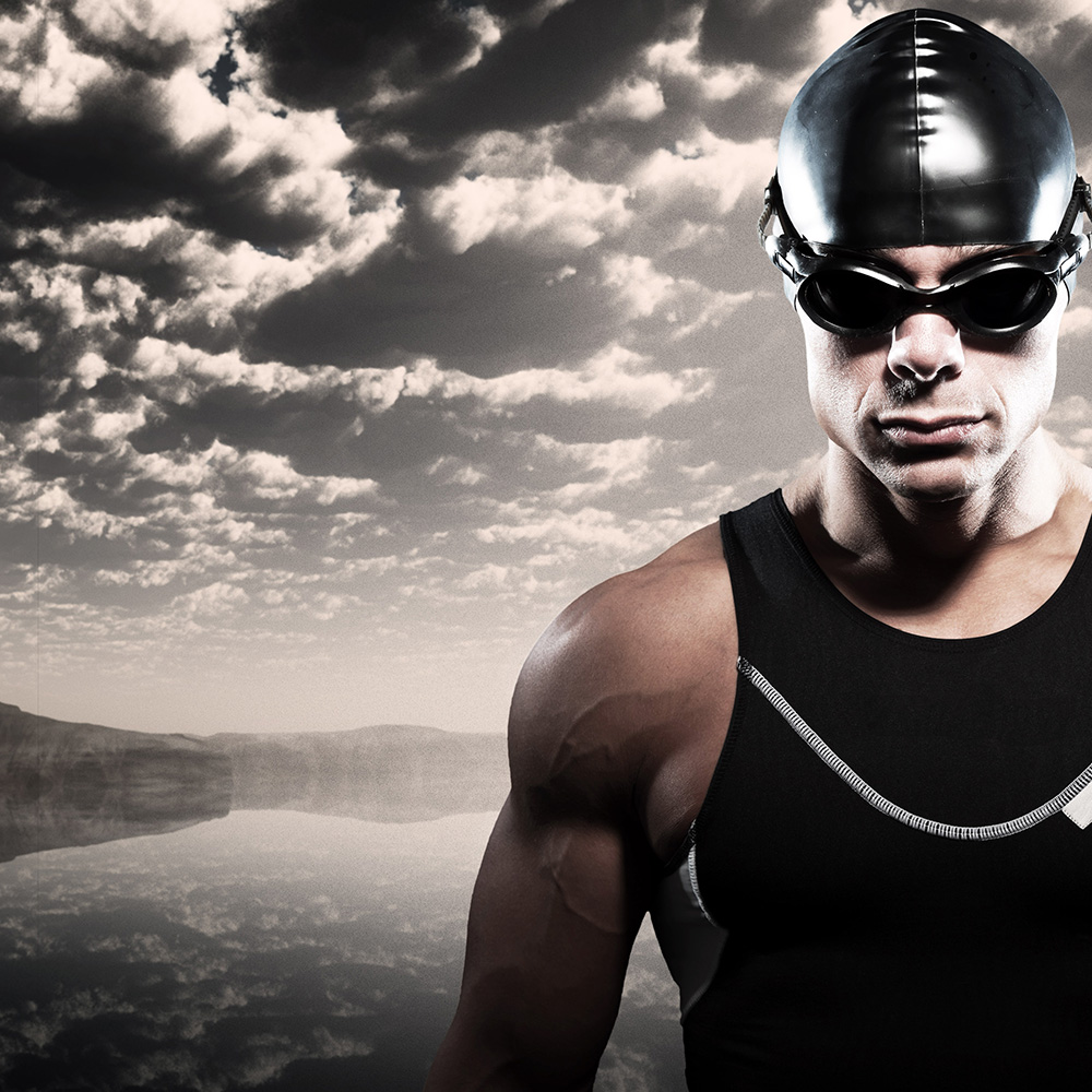 Swimmer triathlon man with cap and glasses outdoor at rough sea with stormy dark sky. Extreme fitness sport.